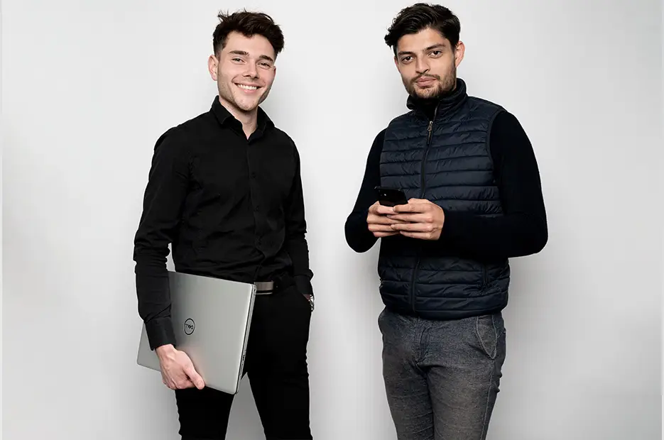 deux étudiant de face, un avec son ordinateur et le second avec son téléphone