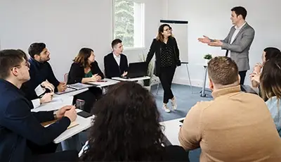 Groupe d'étudiants en classe avec une jeune homme et une jeune femmes debout en train de présenter leur projet