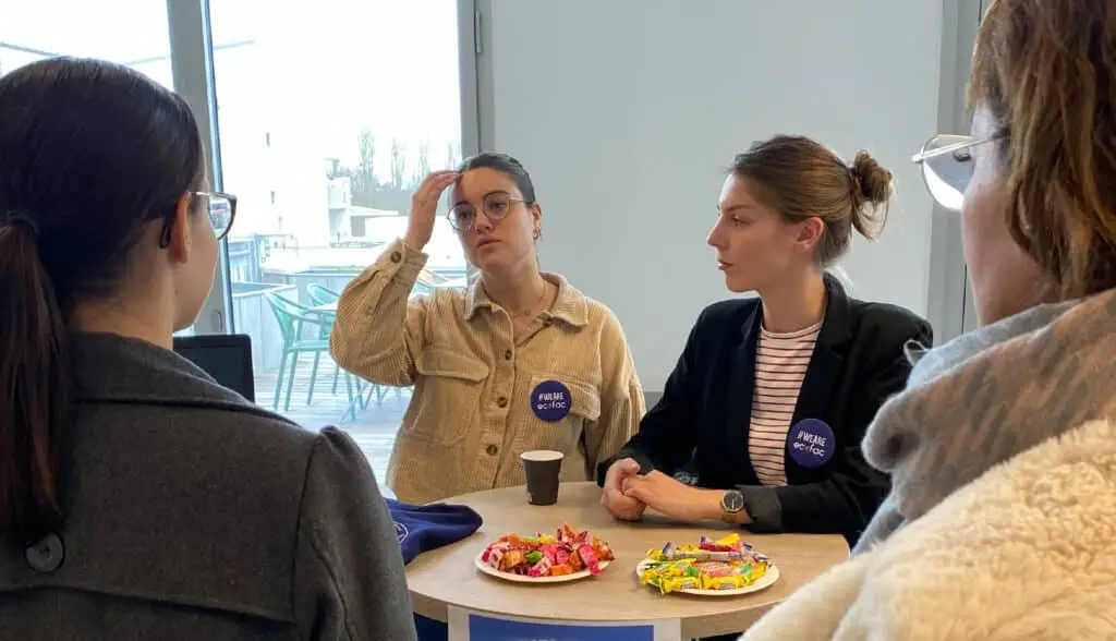 2 étudiantes d'Ecofac qui discutent avec une candidate lors d'une journée portes ouvertes, autour d'un café et de bonbons.