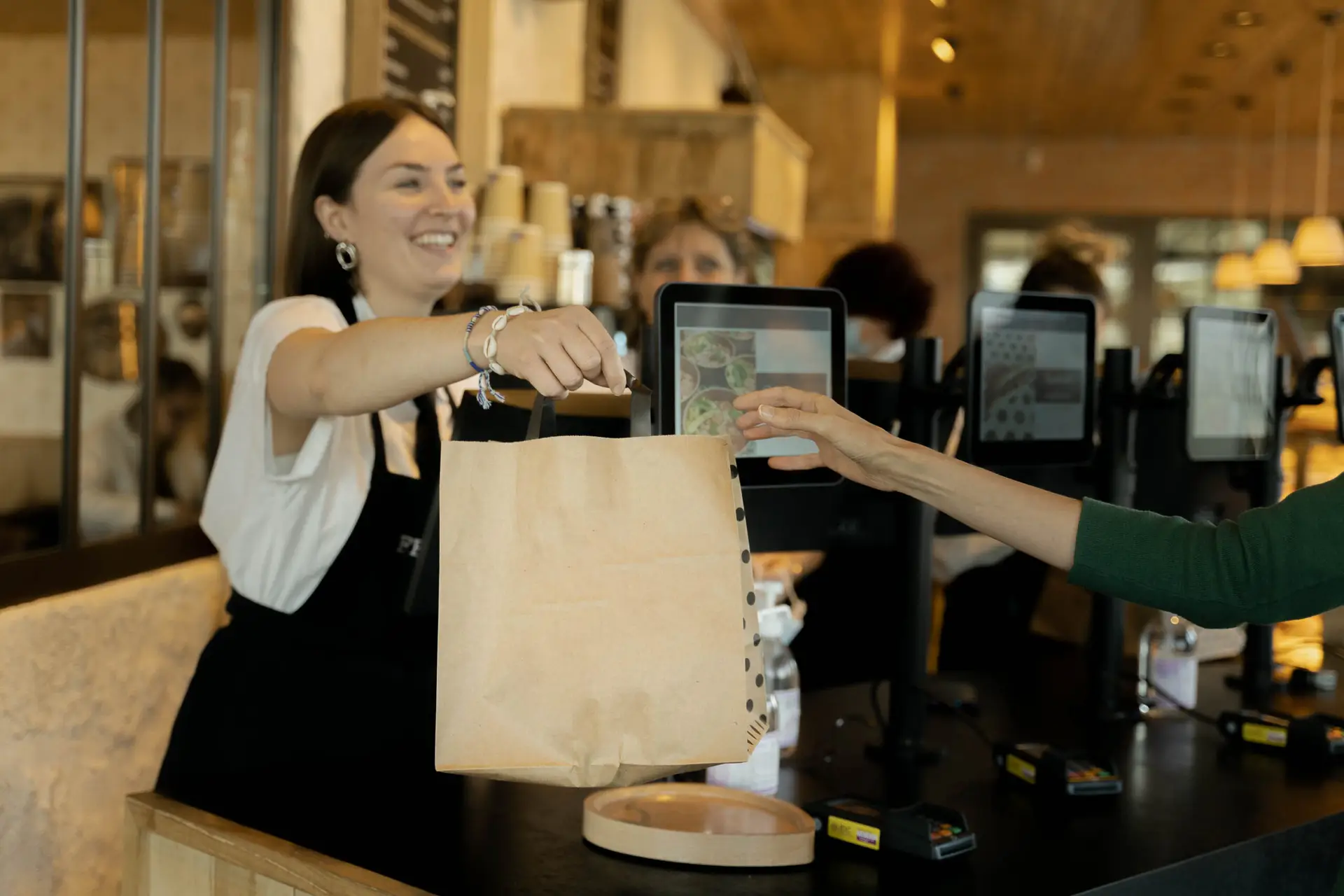 Photo d'une étudiante Ecofac en alternance dans une boulangerie qui tend un sac à une cliente.