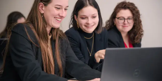 3 étudiantes Ecofac souriantes qui échangent face à leur ordinateur