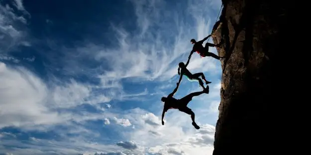 groupe de personne grimpant une falaise pour illustrer l'entraide entre collaborateur