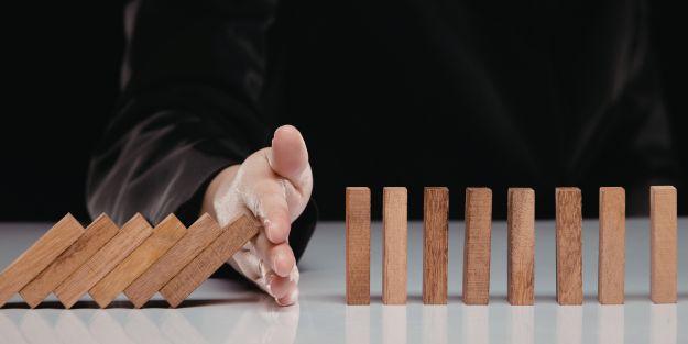 une main qui bloque la chute de domino pour symboliser la prévention des risques